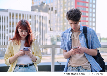 Teenage friends guy and girl using smartphones, urban outdoor Teenage friends guy and girl using smartphones, urban outdoor 114279783