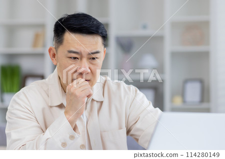 Mature Asian businessman in thoughtful pose, sitting at his office desk. This image captures a moment of deep concentration and decision-making in a professional setting. 114280149