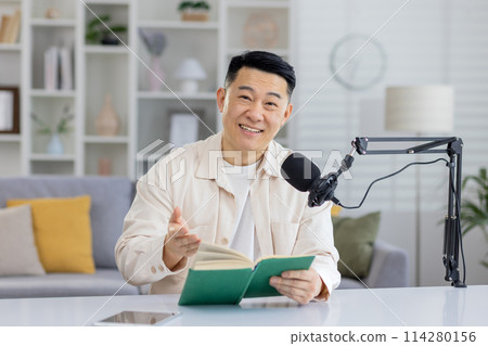A focused individual conducting a virtual book reading session with a microphone and a book in a home environment. 114280156