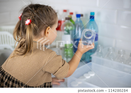 The daughter, under the supervision of her mother, helps sort plastic bottles for recycling. Cute little girl happily puts plastic into containers with a recycling sign. Zero waste concept. The daughter, under the supervision of her mother, helps sort plastic bottles for recycling. Cute little girl happily puts plastic into containers with a recycling sign. Zero waste concept. 114280284