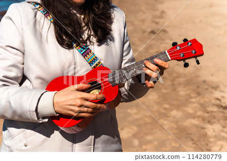 A woman holding a red ukulele in her hands 114280779