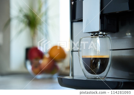 Fresh espresso at morning. Coffee machine in kitchen, close up. Modern coffee maker with freshly brewed coffee in glass cup. Kitchen appliances 114281093