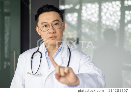 Confident Asian mature male doctor giving professional healthcare advice in a clinic, pointing forward, with stethoscope and blurred background. Confident Asian mature male doctor giving professional healthcare advice in a clinic, pointing forward, with stethoscope and blurred background. 114281507