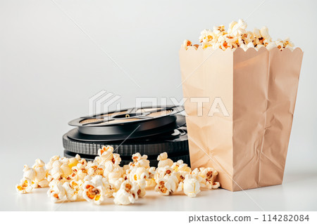 A red and white striped popcorn bucket full of fluffy, buttery popcorn and movie reel isolated on white background 114282084