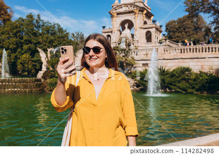 Young female tourist visiting Ciutadella Park in Barcelona. Young traveling woman taking selfie outdoors. Concept of travel, tourism and vacation in city. Use technology concept, Traveling Europe Young female tourist visiting Ciutadella Park in Barcelona. Young traveling woman taking selfie outdoors. Concept of travel, tourism and vacation in city. Use technology concept, Traveling Europe 114282498