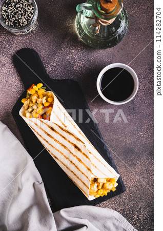 Appetizing burrito in a tortilla made of chicken, corn and peppers on a board top and vertical view Appetizing burrito in a tortilla made of chicken, corn and peppers on a board top and vertical view 114282704