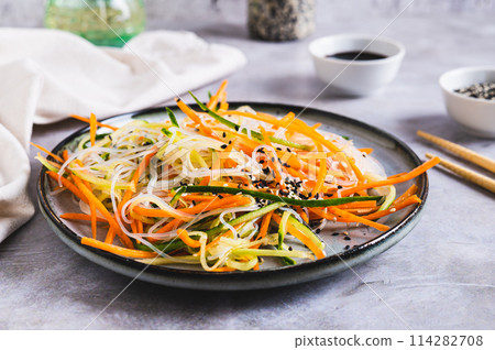 Appetizing salad of funchose, carrots, cucumber and sesame on a plate on the table Appetizing salad of funchose, carrots, cucumber and sesame on a plate on the table 114282708