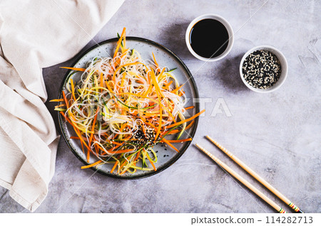 Appetizing salad of funchose, carrots, cucumber and sesame on a plate on the table top view Appetizing salad of funchose, carrots, cucumber and sesame on a plate on the table top view 114282713