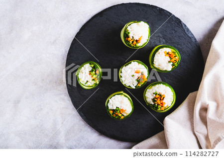 Close up of vegetable sushi made of rice, cucumber and carrots on a slate board top view Close up of vegetable sushi made of rice, cucumber and carrots on a slate board top view 114282727