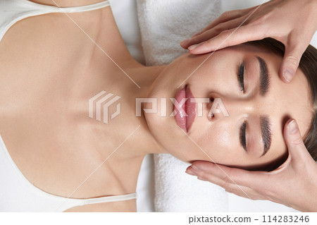 Face massage. Beautiful of young woman getting spa massage treatment at beauty spa salon.Spa skin and body care. Facial beauty treatment.Cosmetology. 114283246
