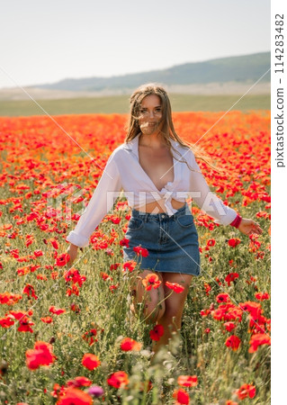 Happy woman in a poppy field in a white shirt and denim skirt with a wreath of poppies on her head posing and enjoying the poppy field. Happy woman in a poppy field in a white shirt and denim skirt with a wreath of poppies on her head posing and enjoying the poppy field. 114283482
