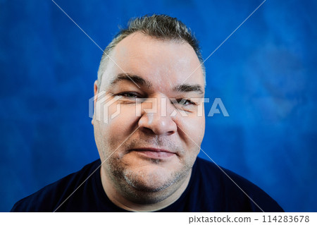Sly look of plump white man over 40 years old on blue background, close-up of his face. Sly look of plump white man over 40 years old on blue background, close-up of his face. 114283678