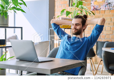 Satisfied relaxed young man looking at laptop screen while sitting in coworking cafe Satisfied relaxed young man looking at laptop screen while sitting in coworking cafe 114283971