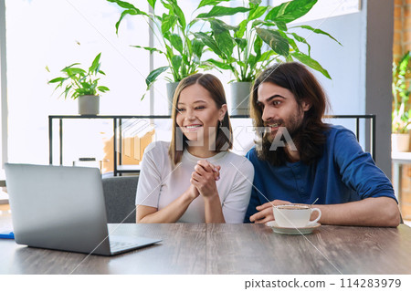 Happy surprised young couple looking at laptop together while sitting in cafeteria 114283979