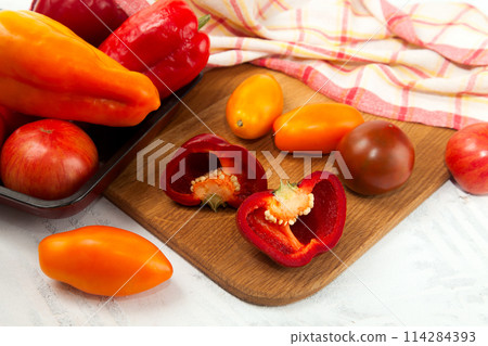 Cutting board with assort of different tomatoes and bell pepper on white wooden background.. 114284393