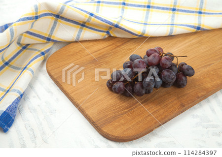 Cutting board with bunch of organic black grapes on white wooden background.. Cutting board with bunch of organic black grapes on white wooden background.. 114284397