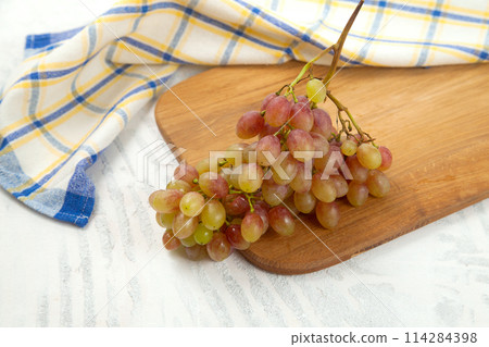 Cutting board with bunch of organic pink grapes on white wooden background.. 114284398