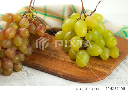 Cutting board with bunch of organic green and pink grapes on white wooden background.. Cutting board with bunch of organic green and pink grapes on white wooden background.. 114284406