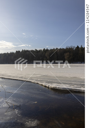 the ice-covered surface of the river in the winter season 114284547