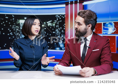 Diverse broadcasters reading daily headlines in newsroom, using media outlets papers to present latest information and updates about events. Journalists team reporting live for tv newscast. 114285048