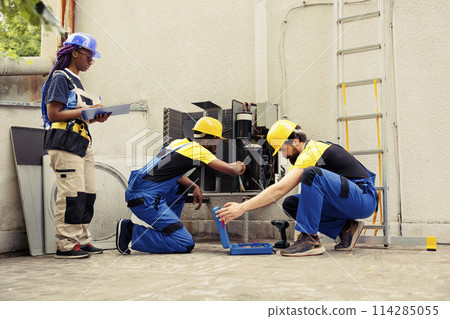 Diverse crew contracted by home owner to fix broken air conditioner. Coworking mechanics analysing broken blower fan causing frozen evaporator coil, resulting in poor airflow Diverse crew contracted by home owner to fix broken air conditioner. Coworking mechanics analysing broken blower fan causing frozen evaporator coil, resulting in poor airflow 114285055