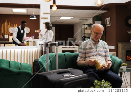 Speaking to young concierge at main desk of luxury resort is caucasian female traveller. While old woman completes booking process at counter an elderly man reading a book relaxes in hotel lobby. Speaking to young concierge at main desk of luxury resort is caucasian female traveller. While old woman completes booking process at counter an elderly man reading a book relaxes in hotel lobby. 114285125