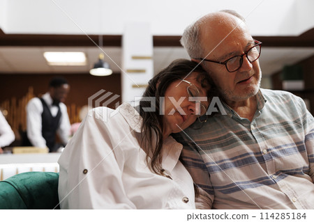 Two senior adults sleeping on cozy couch in a luxurious lounge area while waiting for check-in procedure. After long flight, caucasian elderly couple resting on comfortable sofa. Close up shot. 114285184