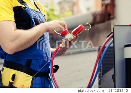 Experienced wireman doing annual air conditioner maintenance, assembling pressure measurement device before starting work. Licensed serviceman refilling cooling system refrigerant tank Experienced wireman doing annual air conditioner maintenance, assembling pressure measurement device before starting work. Licensed serviceman refilling cooling system refrigerant tank 114285240