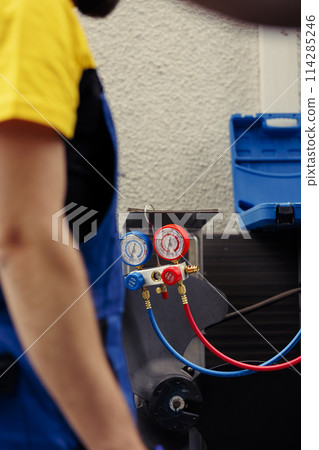 Adept repairman hired to check outdoor hvac system refrigerant tank in need of maintenance, using manometers. Licensed serviceman with ac gauges vacuum pump looking at air conditioner freon levels 114285246