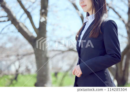 A woman in a suit walking along a row of cherry blossom trees 114285304