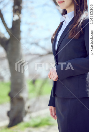 A woman in a suit walking along a row of cherry blossom trees 114285306