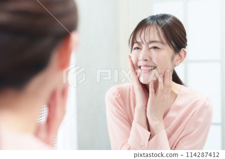 Woman looking at the mirror at the sink, anti-aging, skin care Woman looking at the mirror at the sink, anti-aging, skin care 114287412