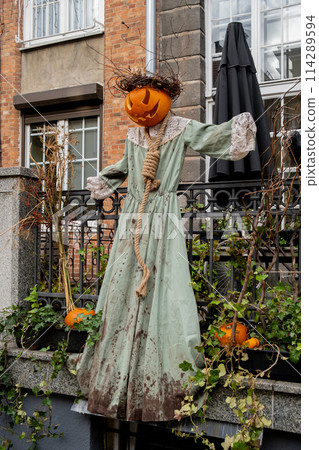 Exterior Beautiful atmospheric halloween scary scarecrow pumpkin decorated on porch. Autumn leaves and fall flowers celebration holiday Thanksgiving October season outdoors 114289594