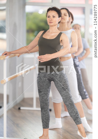 Group of female beginners performing batman tandu at barre 114289775
