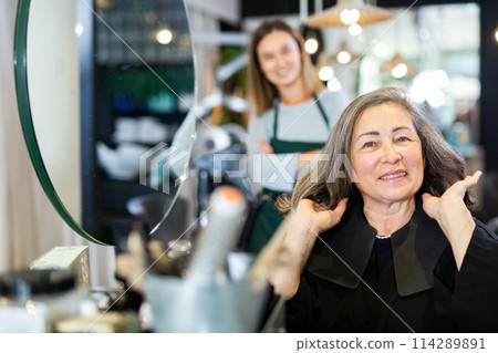Aged woman looking satisfied with new hairdo in hairdressing salon 114289891