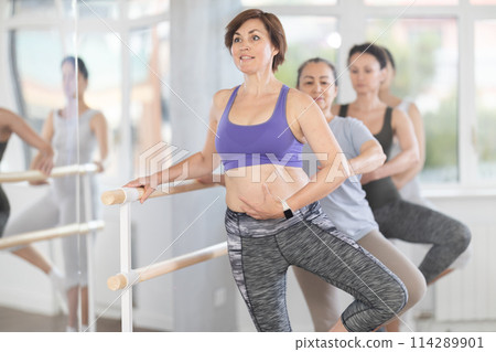 Woman, along with like minded people, is engaged in ballet studio for amateurs Woman, along with like minded people, is engaged in ballet studio for amateurs 114289901