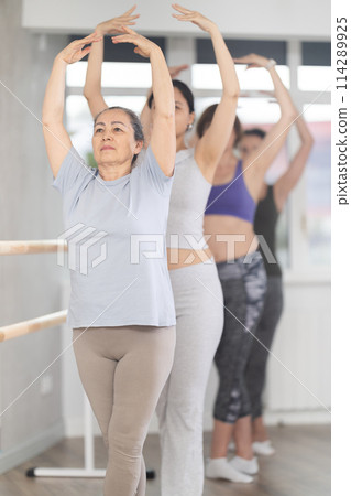 Group of women stand in fifth position at barre 114289925
