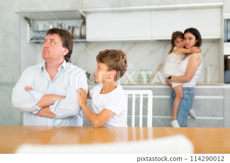Offended father sitting at the kitchen table being hugged by son Offended father sitting at the kitchen table being hugged by son 114290012