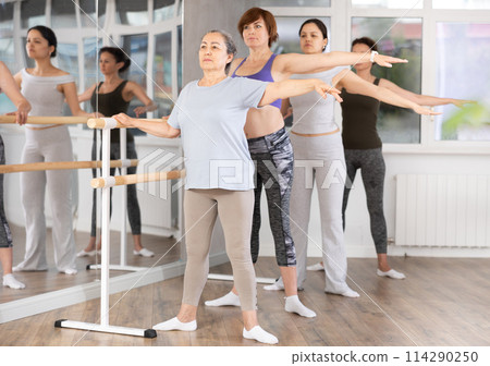 Group of women stand in second position at barre 114290250