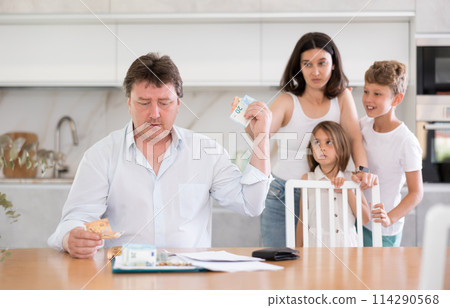 Thoughtful man sitting at the kitchen table giving money to his wife Thoughtful man sitting at the kitchen table giving money to his wife 114290568