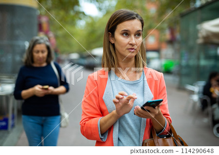 Interested female tourist using phone while walking through city 114290648