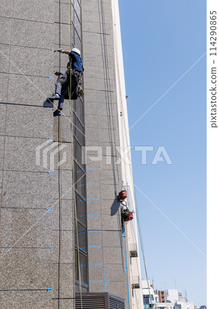 一名工人掛在繩子上修理建築物的外牆 114290865