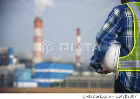 Backside Electrician engineer man hand holding White hardhat at Power stations manufacturing electrical plant. Technician worker blue hardhat helmet Engineer with steam smokestack industry background Backside Electrician engineer man hand holding White hardhat at Power stations manufacturing electrical plant. Technician worker blue hardhat helmet Engineer with steam smokestack industry background 114292307