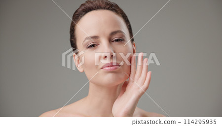 Beauty, health, cosmetics, anti-aging therapy and skin care concept - young beautiful brunette Caucasian woman touching face and looking at camera 114295935