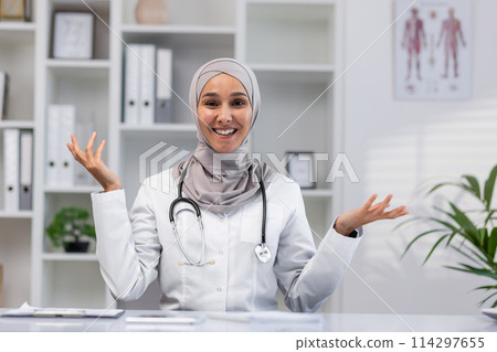 A cheerful Muslim female doctor wearing a hijab speaks with a positive gesture in a modern medical office setting, representing approachable healthcare. A cheerful Muslim female doctor wearing a hijab speaks with a positive gesture in a modern medical office setting, representing approachable healthcare. 114297655