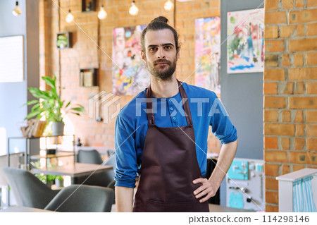 Young man worker, owner in apron looking at camera in restaurant, coffee shop 114298146