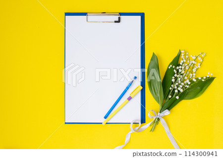 A tablet with paper as a template with a place to copy on a yellow table with lilies of the valley 114300941