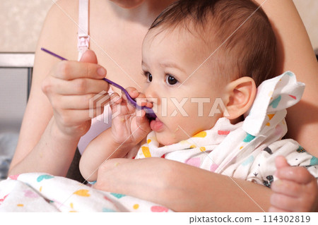 Portrait of little baby boy eating food. Baby with a spoon in feeding chair. Cute baby eating first meal 114302819