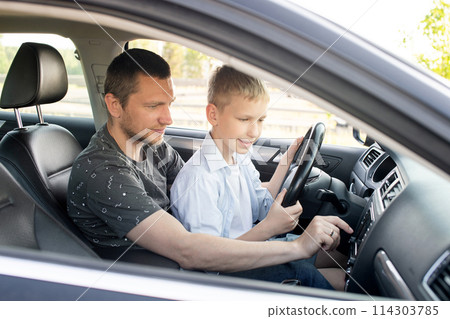 Dad and son in the front seat of a car driving a black car Dad and son in the front seat of a car driving a black car 114303785