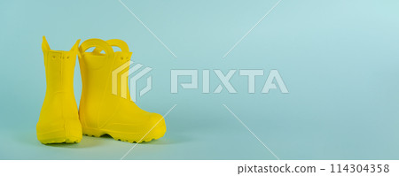 Yellow kids gumboots on blue background. Pair of yellow rubber boots. Banner, copy space Yellow kids gumboots on blue background. Pair of yellow rubber boots. Banner, copy space 114304358